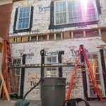 House exterior renovation with ladders and Tyvek